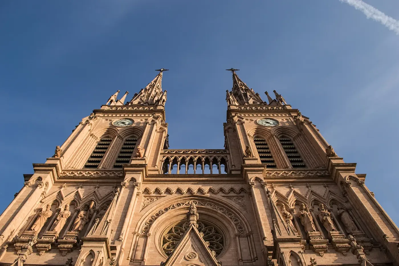 Fachada da basílica de Nossa Senhora de Luján vista de baixo, com as duas torres góticas de relógio contra o céu azul.